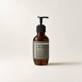 Commen Nº.15 Patchouli Body Serum, a 270 ml amber pump bottle with an olive label, standing on light paper.