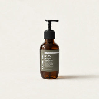 Commen Nº.15 Patchouli Body Serum, a 270 ml amber pump bottle with an olive label, standing on light paper.