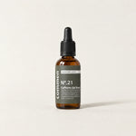 Commen Nº.21 Caffeine Gel Boost, an amber dropper bottle with a dark label, standing on light paper.