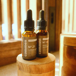 Commen Nº.21 Caffeine Gel Boost and Nº.22 Ginkgo Antioxidant Boost, two amber dropper bottles on a teak stand.