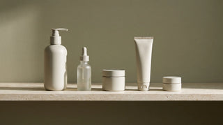Five unbranded skincare containers lined up in order on a travertine shelf against an olive wall.